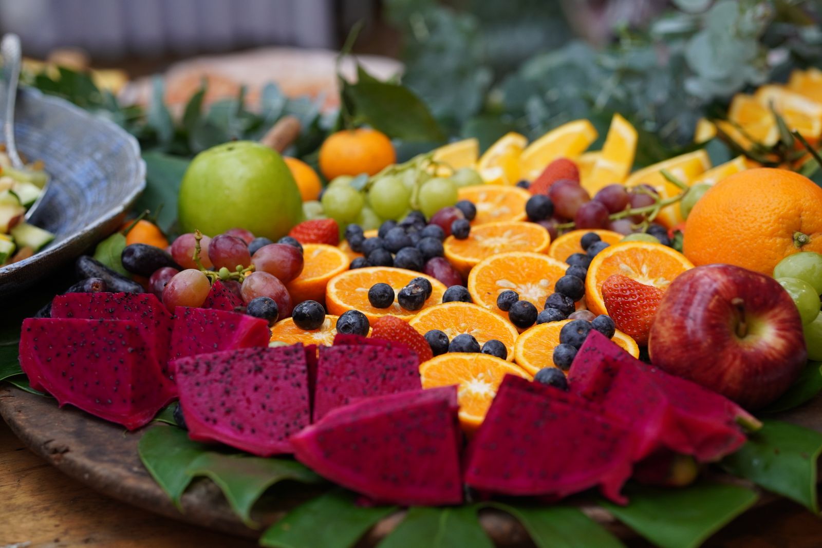 Morceaux de fruits colorés disposés en lignes arc-en-ciel dans une grande assiette, sans pics.