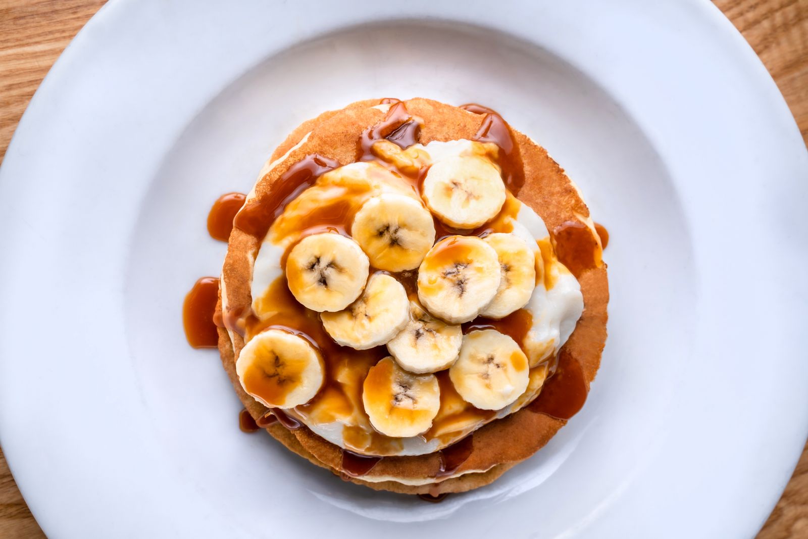 Petite pile de pancakes dorés accompagnée de rondelles de banane et de fruits.